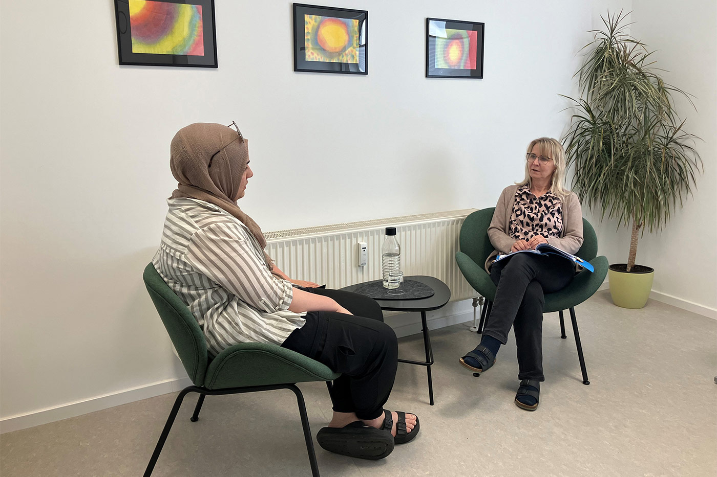 Zwei Frauen sitzen sich an einem kleinen Tisch gegenüber. Die Frau rechts spricht, die Frau links hört zu – Beratungssituation