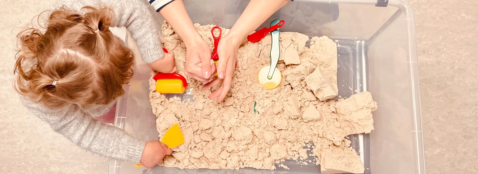 Hände eines Kindes und einer erwachsenen Person spielen zusammen im Sandbehälter