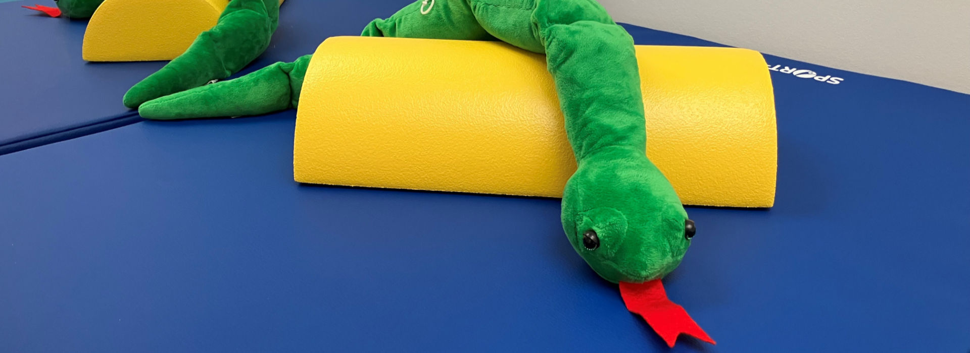Eine grüne Schlange aus Stoff liegt auf einer Turnmatte