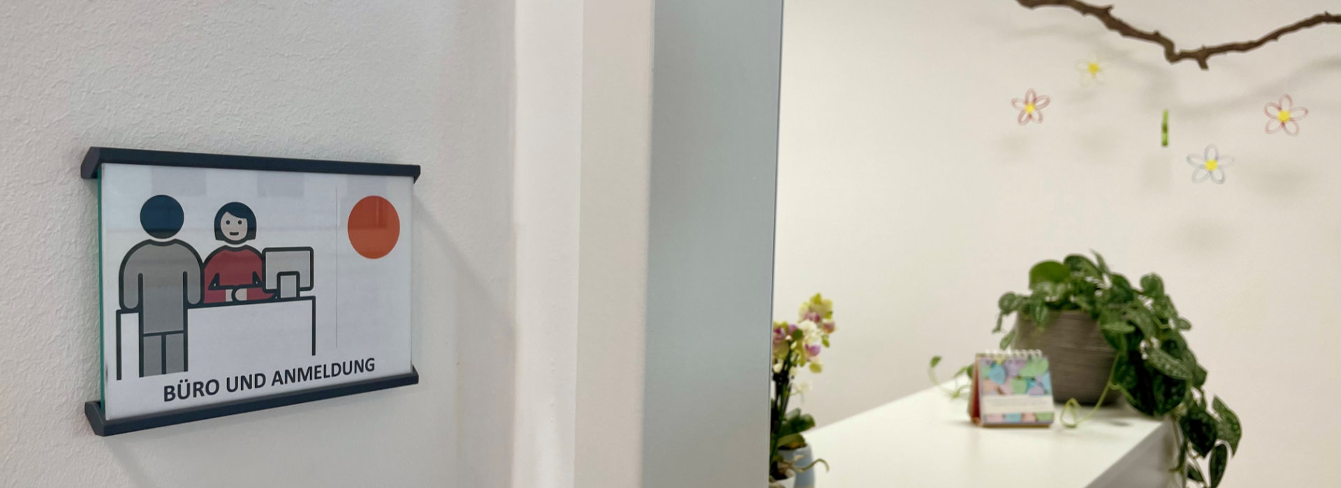 Schild mit der Aufschrift "Büro und Anmeldung" hängt an der Wand, im Hintergrund ist der Empfangstresen