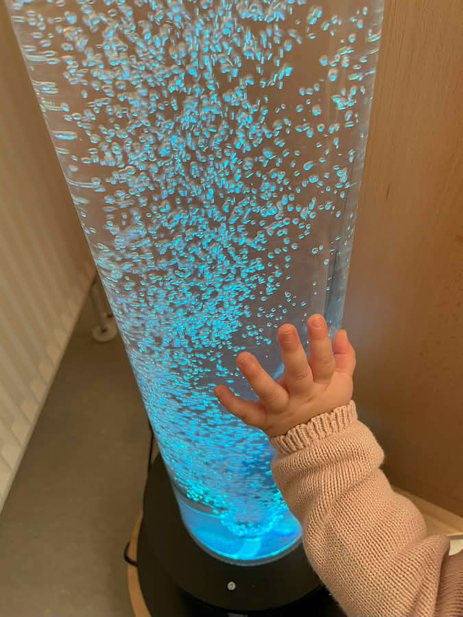 Kinderhand berührt eine mit blauem Wasser gefüllte Plexiglas-Säule mit aufsteigenden Bläschen