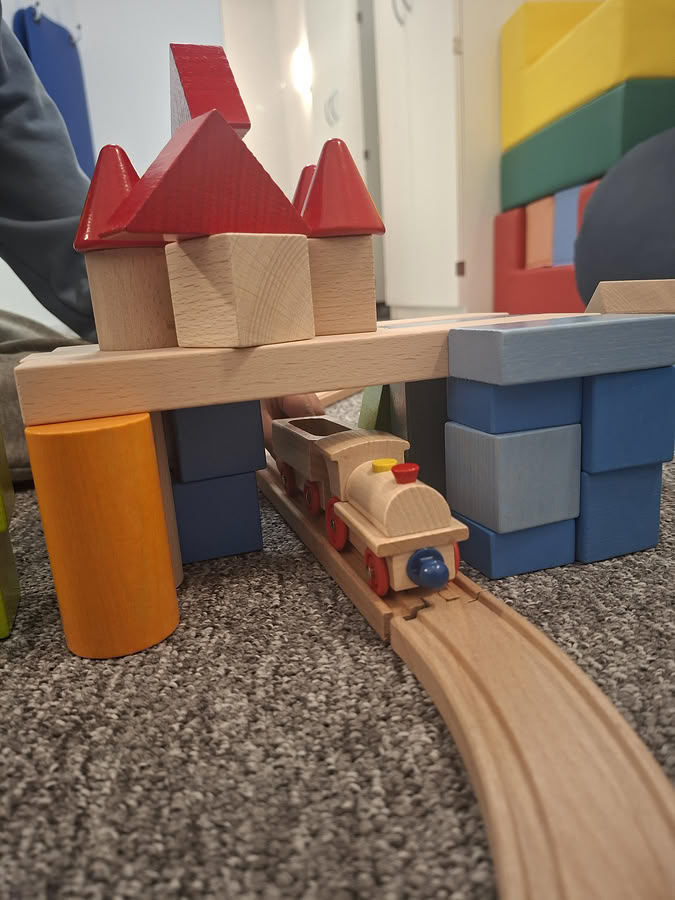 Holzeisenbahn fährt unter einer Brücke aus Bauklötzen durch