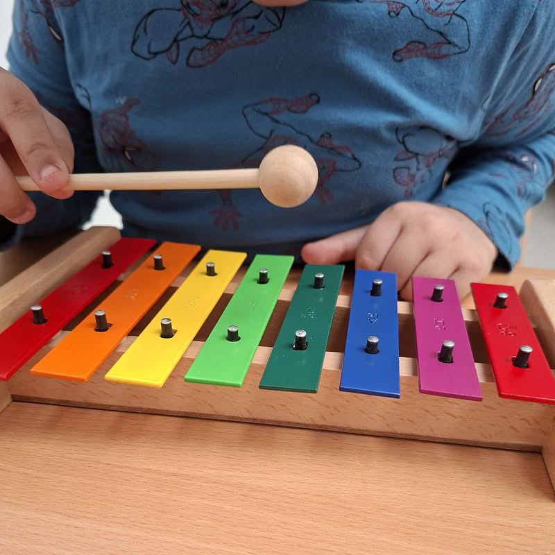 Kind schlägt mit einem Klöppel auf die bunten Klangplatten eines Xylophons