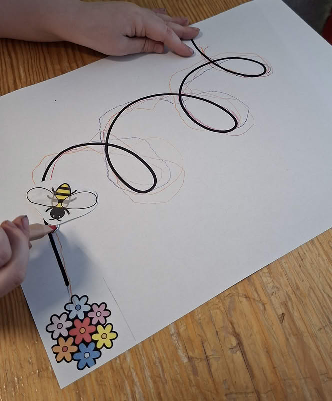 Kinderhand zeichnet einen schwarzen Kringel auf ein weißes Blatt Papier