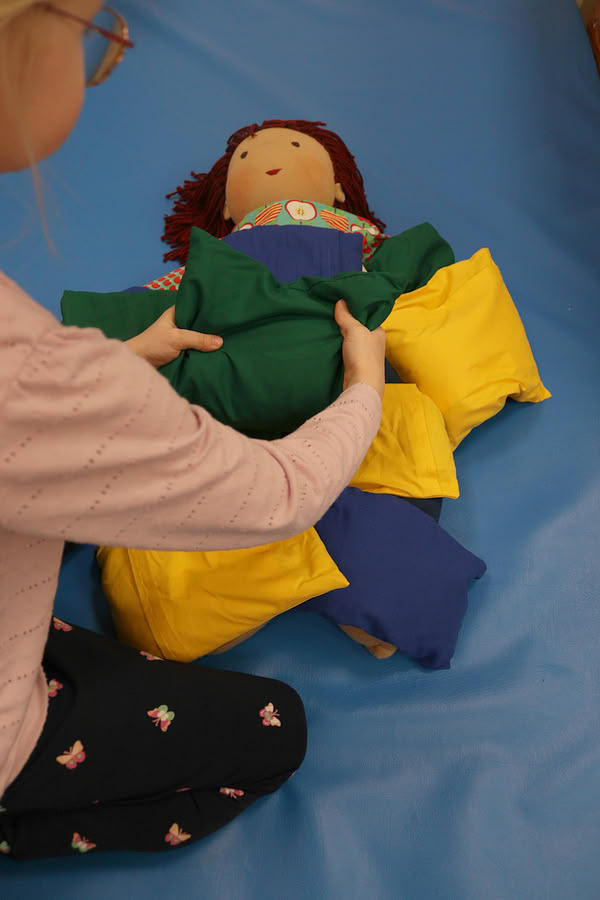 Kind legt kleine Kissen auf eine Stoffpuppe